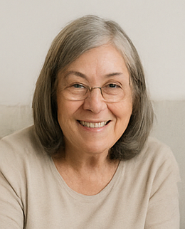 Woman sitting on a couch wearing glasses and a beige sweater.