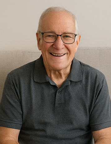 Man wearing glasses and a dark gray polo shirt sitting against a neutral background